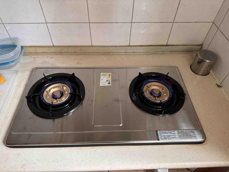 1) 照片顯示一個銀色的雙口瓦斯爐,有兩個黑色的瓦斯爐頭,每個瓦斯爐頭都有藍色的火焰