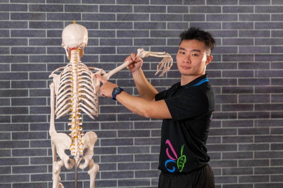 這張照片是一個男人正在研究一個骨骼模型。他正在用手觸摸骨骼的肩胛骨,看起來好像在學習人體結構。