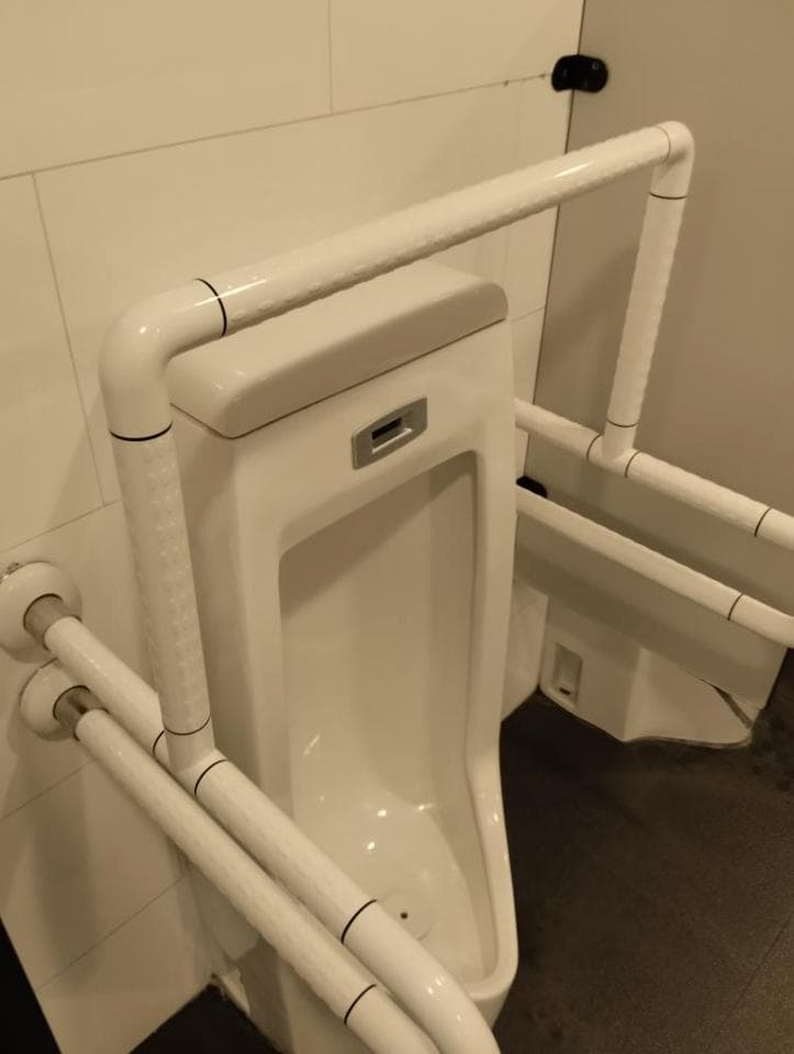 1) 照片顯示一個白色的小便斗,它裝在牆上,並有一個白色的扶手