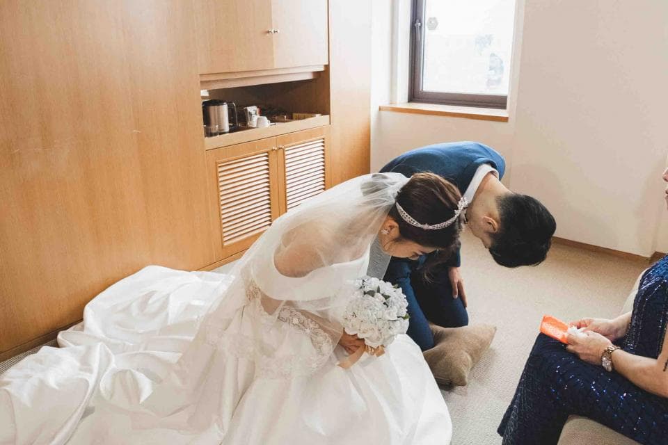 這張照片是新郎跪下向新娘敬茶,新娘手中捧著一束白色的花。