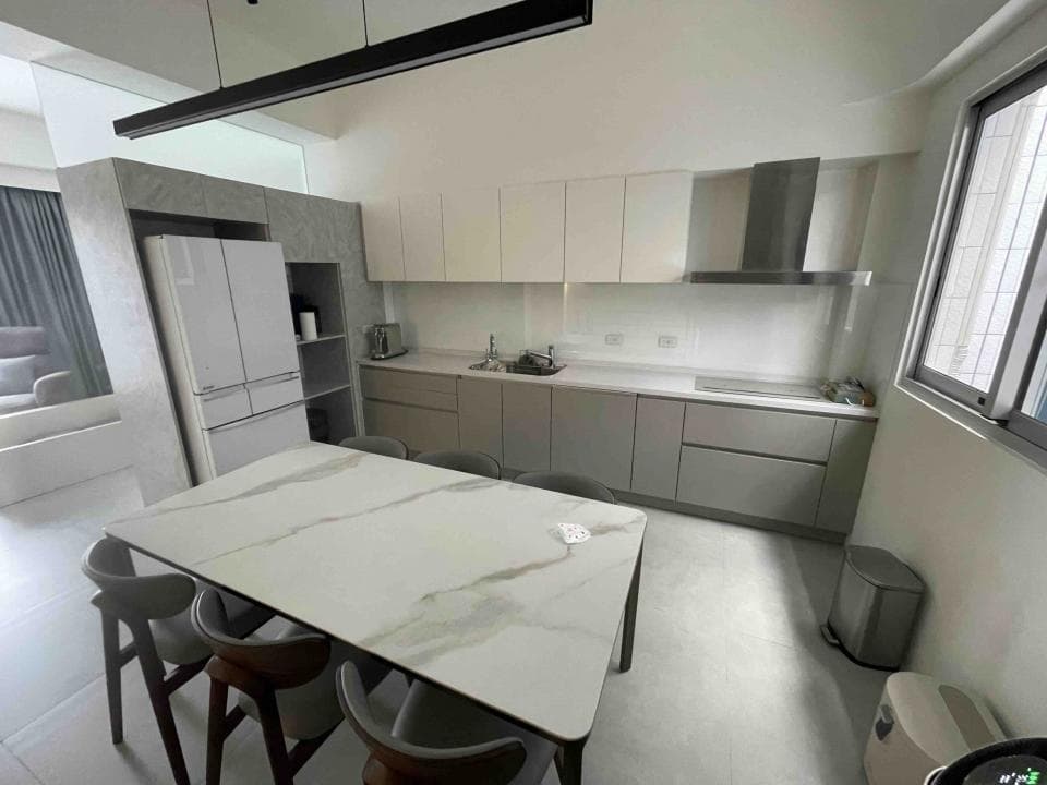 這張照片是現代化的廚房和餐廳空間,餐桌是用白色大理石製成,非常明亮,搭配灰色的櫥櫃,整體感覺非常簡潔。