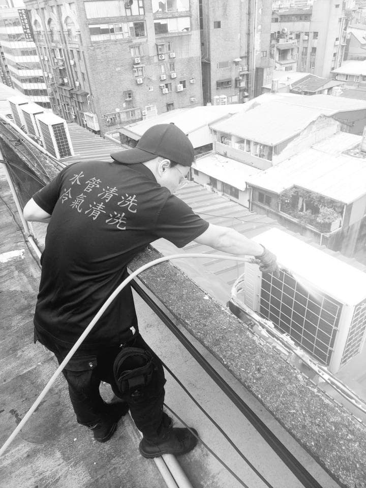 這張照片是一個穿著黑色上衣的男子,他站在建築物的屋頂上,衣服上印著「洗洗洗」。他正在操作一條繩索,看起來像是要從屋頂上往下爬。