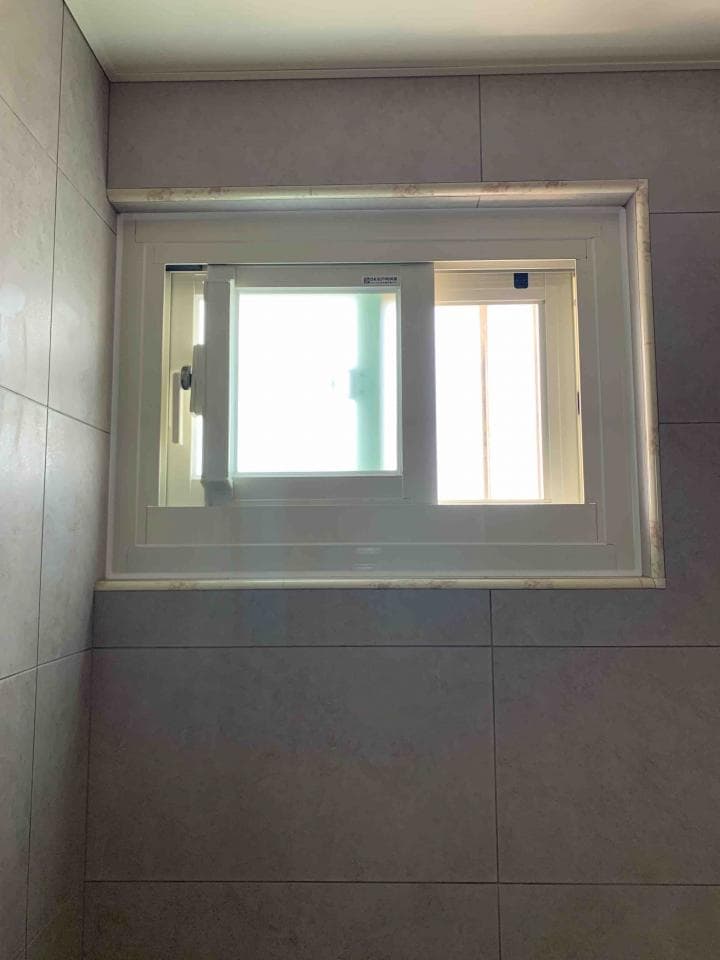 這張照片是一間浴室的牆壁和窗戶。窗戶是白色,並且有兩個玻璃窗格,其中一個窗格是固定式的,而另一個窗格可以打開。