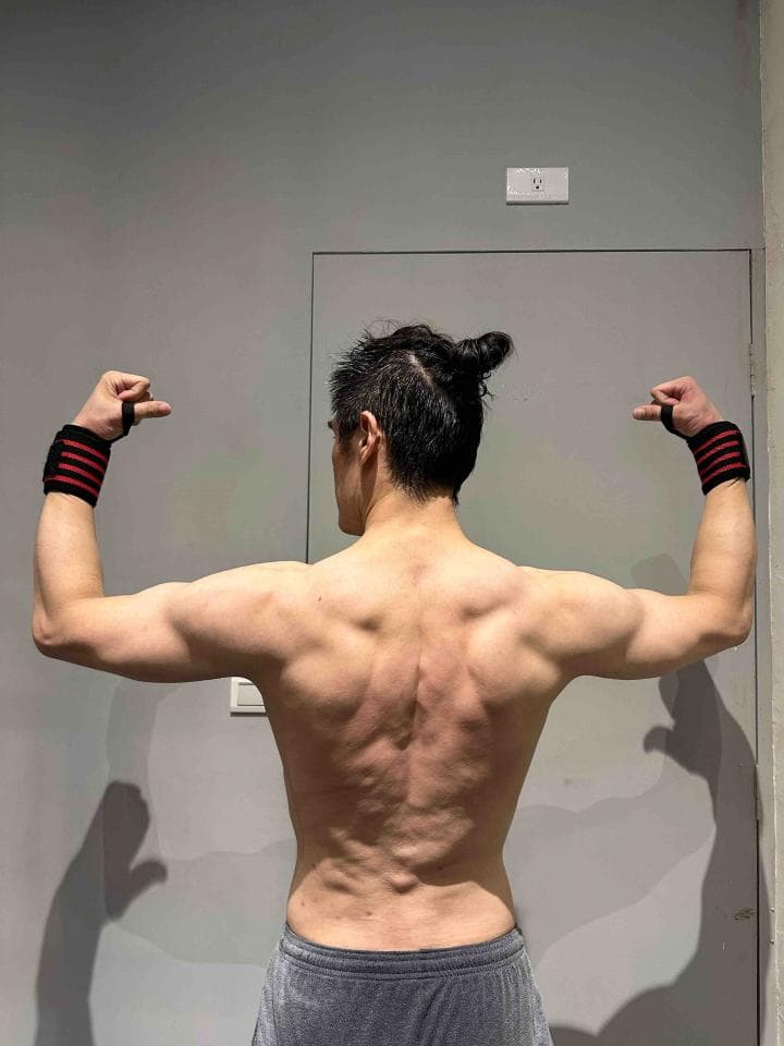 這張「一個男人展示他強壯的背部肌肉」的照片是一個男人,他穿著灰色短褲,雙手舉起,展示他強壯的背部肌肉。