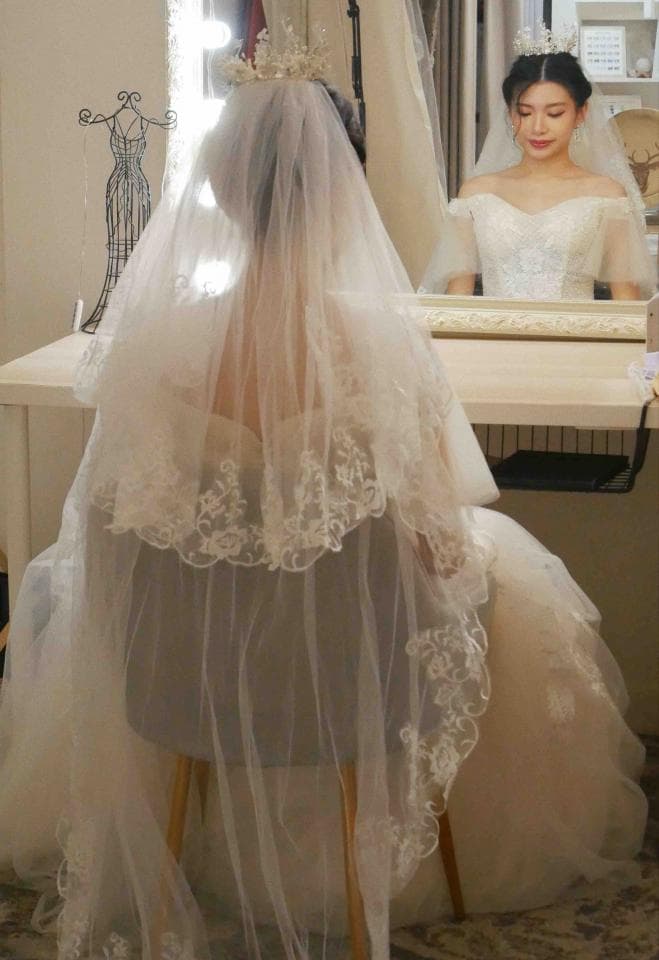 這張照片是一名身穿白色婚紗的女子,她戴著頭紗,頭紗上有精緻的蕾絲花邊,看起來非常美麗。