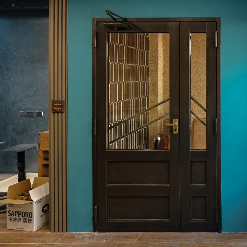 這張照片是一扇深色的雙開門,門上有精緻的格柵設計,門把手是金色的,看起來很高級。門的背景是藍綠色的牆壁,顯得門更加醒目。