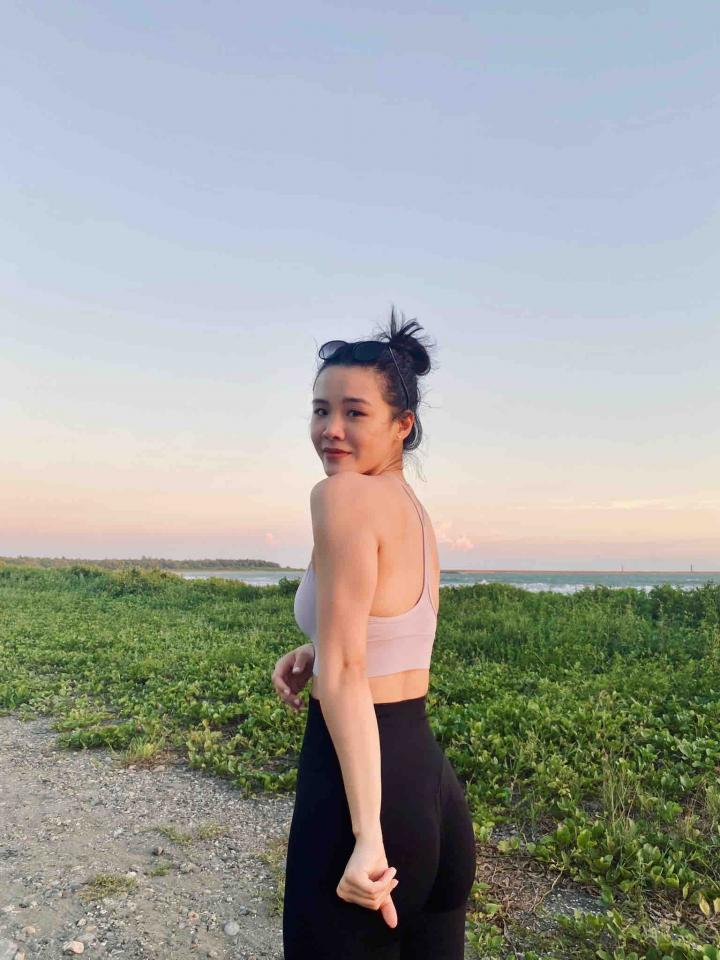 這張照片是一個年輕女子在海邊散步。她穿著運動背心和黑色緊身褲,頭髮綁成馬尾。她正在看著攝影師,並且看起來很放鬆。