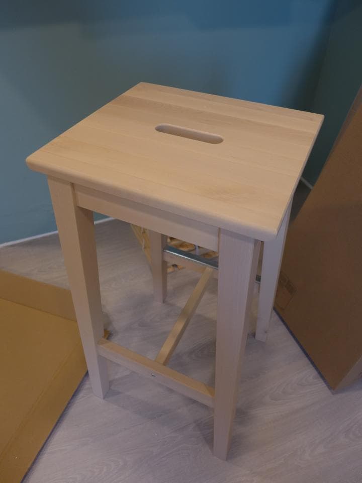 這張照片是一個木頭做的凳子,它有一個長方形的洞,看起來像一個把手。凳子是淺木色的,非常簡潔。