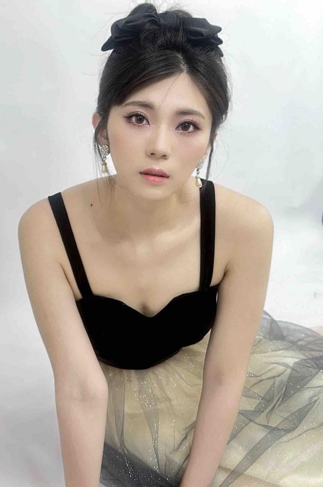 這張照片是一個穿著黑色上衣和金色紗裙的女生。她綁著黑色的髮帶,看起來很有氣質。