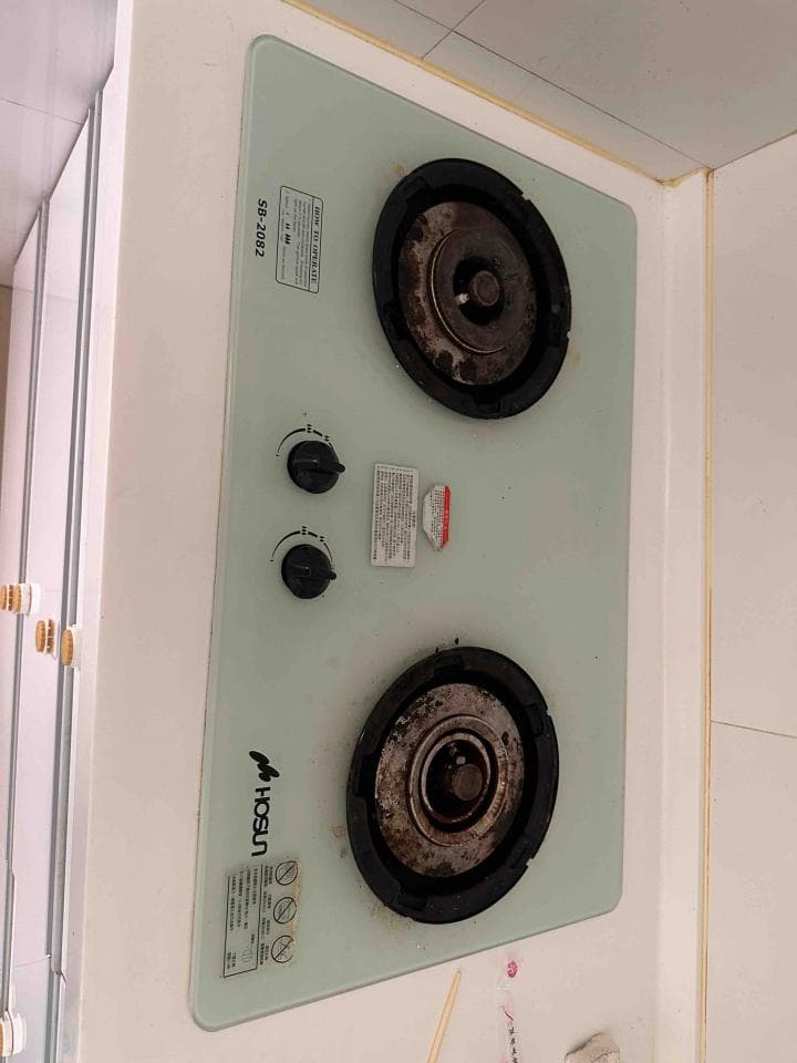 這張照片是一台嵌入式瓦斯爐,有兩個圓形爐頭,旁邊有兩個旋鈕控制火力。爐頭的邊緣有點髒,中間的圓盤也有一些污垢。