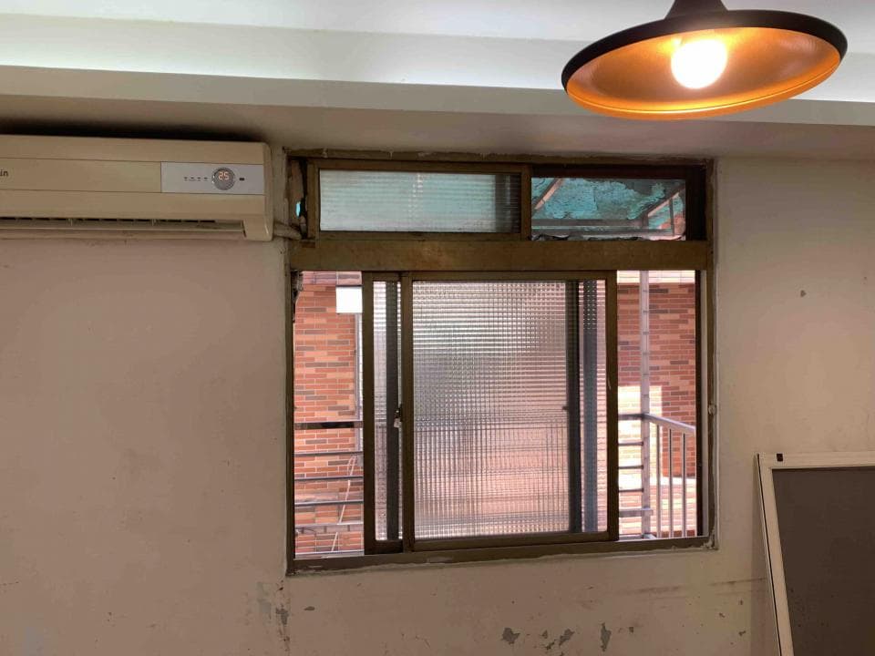 1) 照片顯示一個房間內,房間天花板裝有吊燈,牆壁上裝有冷氣,牆壁上有窗戶,窗外可以看到一棟紅磚建築