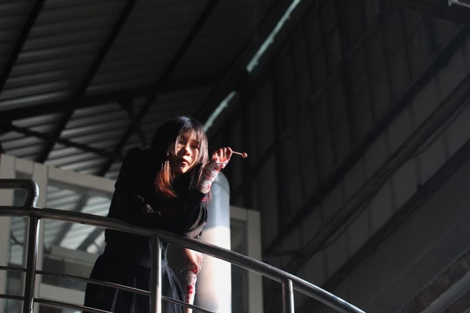 這張照片是一個站在樓梯扶手上方的女孩。她穿著黑色的衣服,用手拿著一根棒子,看起來很酷。