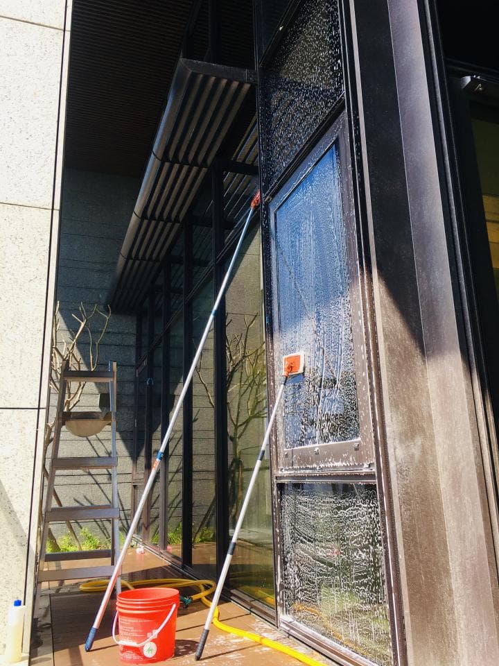 1) 照片顯示一個建築物的外牆,外牆正在清潔,用到了兩支長柄刮刀和一個水桶