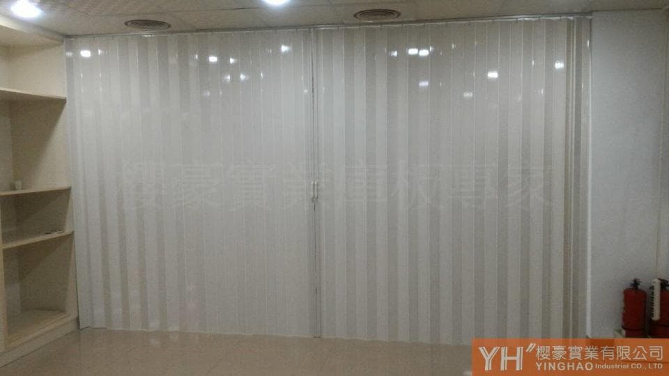 這張照片是一間房間,最顯眼的部分是一道白色摺疊式隔板。隔板由多個垂直的條狀板材組成,可以摺疊收納,形成一個空間隔斷。