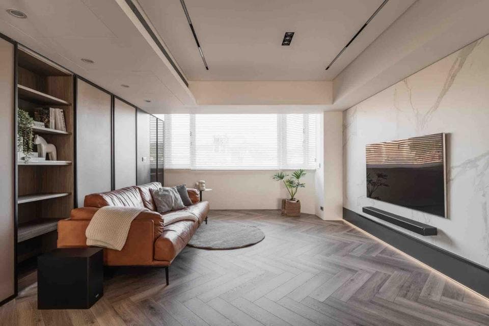 這張客廳的照片是一間寬敞明亮的客廳,有一張皮革沙發、一個大電視、一個書架和一張咖啡桌。