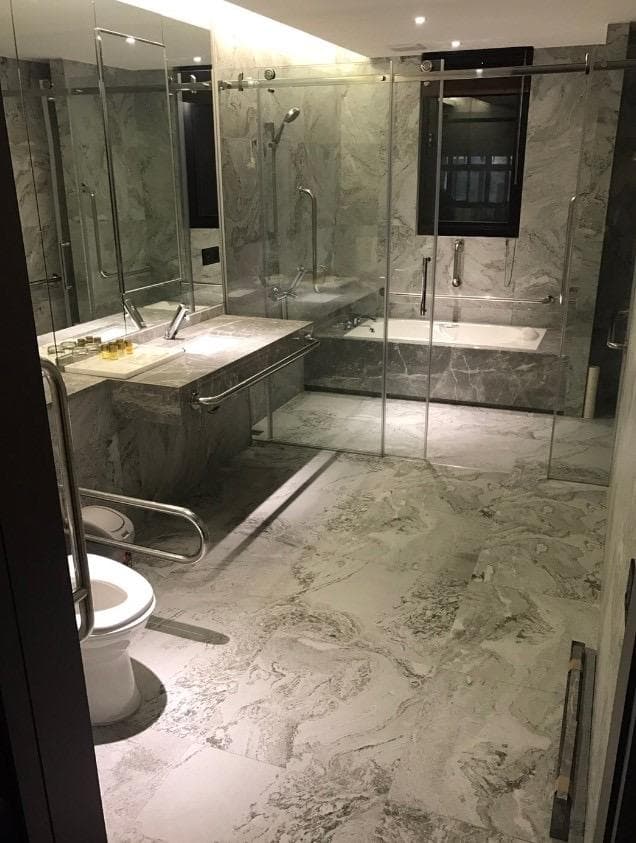 1) 照片顯示一間現代化浴室,浴室裡有馬桶、洗手台、鏡子以及淋浴間,浴室地板和牆壁使用白色大理石,地板上有明顯的紋理