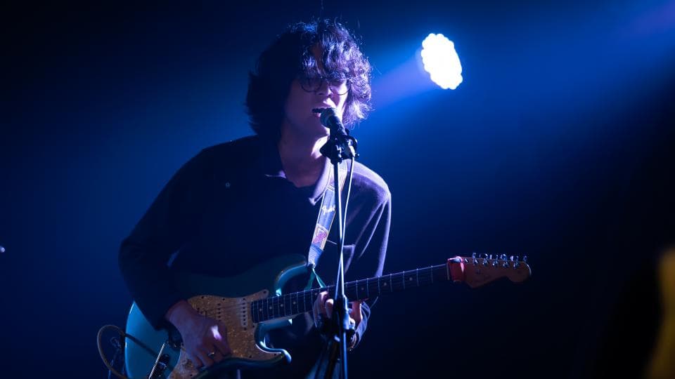 這張「音樂表演」的照片是一個歌手在舞臺上表演,他拿著吉他唱歌,舞臺燈光照耀著他。