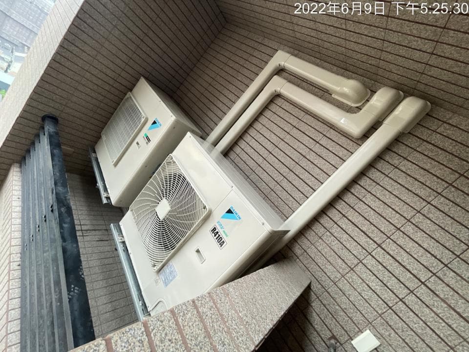 1. 照片顯示兩台室外機安裝在牆壁上,室外機上連接著排水管,牆壁上是磁磚