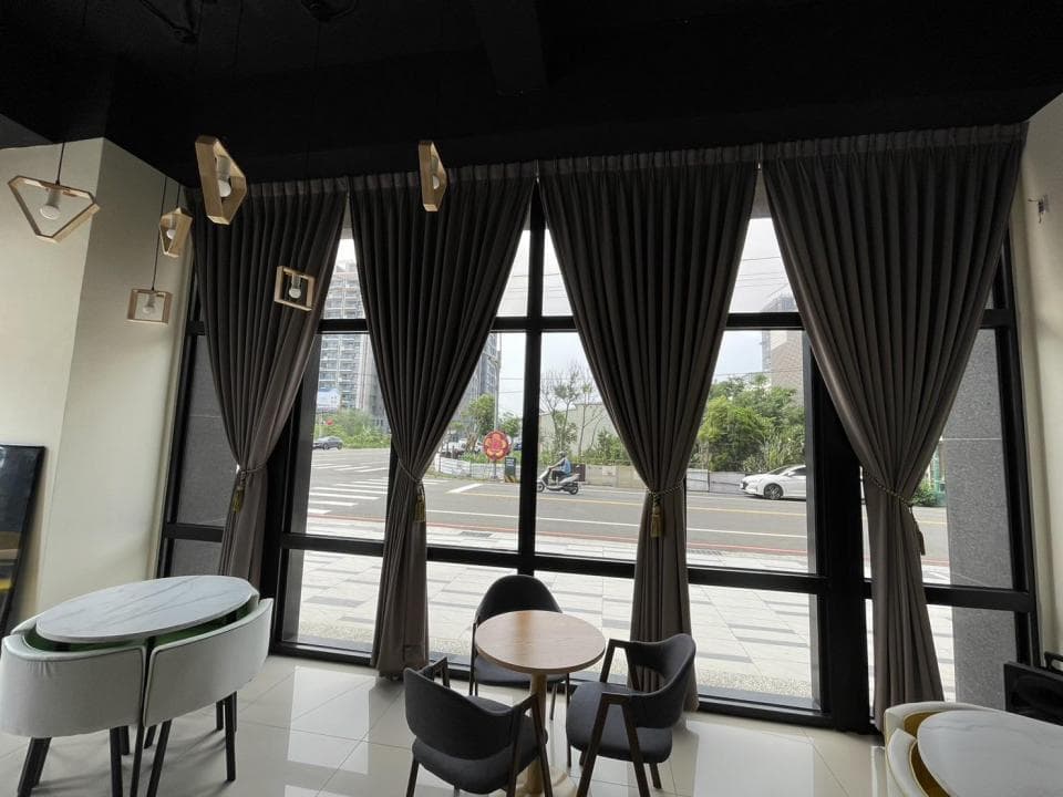 1) 照片顯示一個現代風格的餐廳,室內有大型落地窗,窗戶上掛著灰色窗簾,窗戶外是一條街道,街道上停著汽車