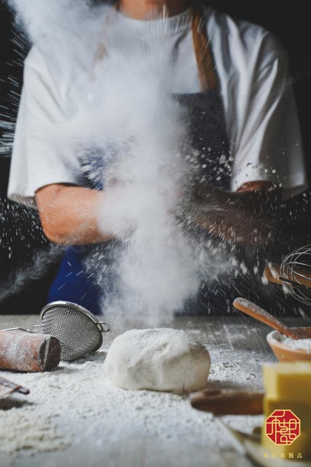 這張「麵粉」的照片是一位穿著圍裙的廚師,正在用雙手拍打麵粉,周圍佈滿了飛揚的麵粉,畫面充滿動感。