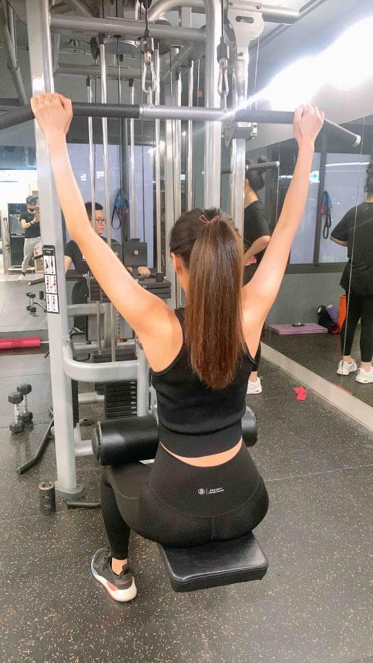 這張照片是一個女性在健身房做拉背運動,她專注於拉動拉力器,手臂伸直並用力,呈現出積極努力的健身狀態。