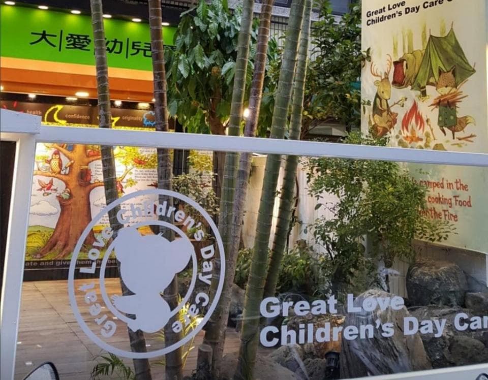 這張「Great Love Children's Day Care」的照片是一個兒童託兒所的外部,照片中可以看到招牌、綠色植物以及一些裝飾。