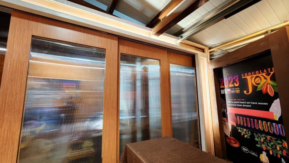 這張「室內」的照片是一個木製的房間,房間裡有兩扇玻璃門,門上有條紋狀的設計,在右邊牆壁上有一張「巧克力」的廣告海報。