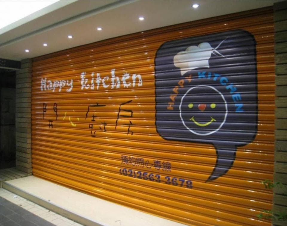 這張照片是餐廳的卷閘門,上面寫著“Happy Kitchen”的字樣,並有一個笑臉圖案的氣泡,看起來很可愛,很有吸引力。