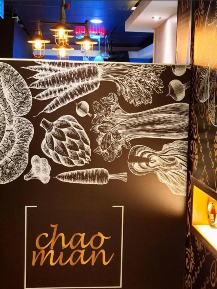 這張「餐廳」的照片是一個有「chao mian」字樣的店面,牆上裝飾著素描風格的蔬菜圖案,例如「胡蘿蔔」和「花椰菜」。