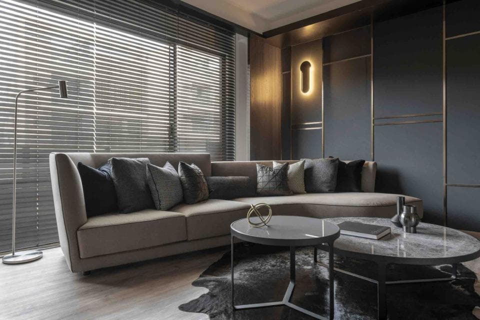 這張「客廳」的照片是一個現代化的空間,有灰色的沙發、兩張圓形咖啡桌和一個落地燈。房間的牆壁是深色,窗戶配有百葉窗。