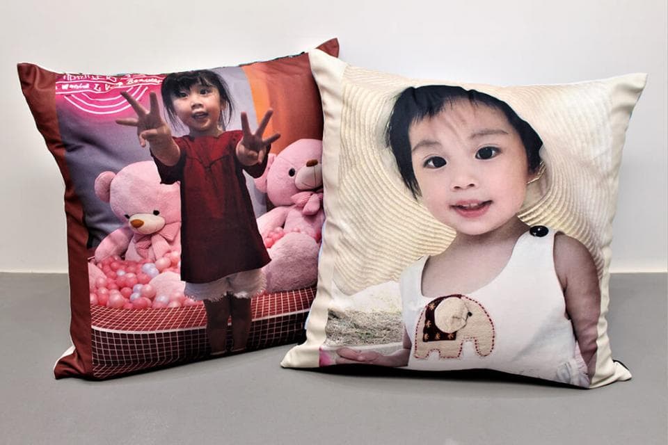 這張「兩個抱枕」的照片是,左邊抱枕印著一個小女孩,她穿著紅色的衣服,站在粉紅色的球池裡;右邊抱枕印著一個戴著帽子的小女孩,她穿著白色的衣服,面帶微笑。
