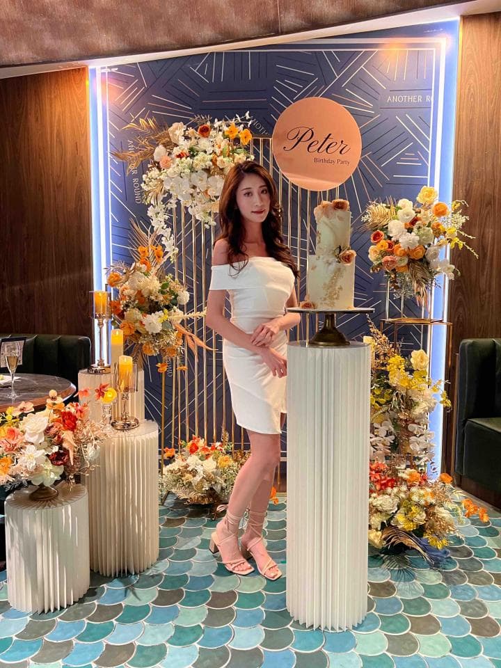 這張「婚禮佈置」的照片是一對新人結婚的場景,背景是藍色的牆面,上面有很多金色的裝飾,中間放著一個寫著「Peter」的圓形招牌。新娘穿著白色禮服,站在蛋糕旁,看起來很漂亮。地上鋪著藍色的馬賽克磁磚,還有很多鮮花擺設,增添喜慶的氛圍。