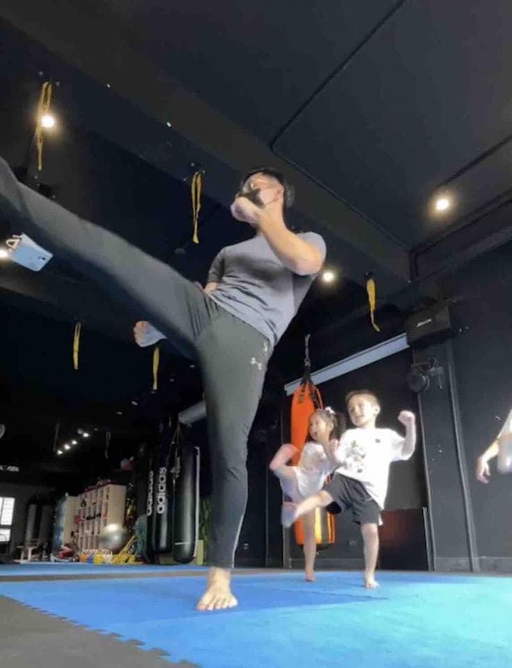 這張照片是一個男人在拳擊館教兩個小孩踢腿。他正在做示範,而兩個小孩也正在努力模仿。