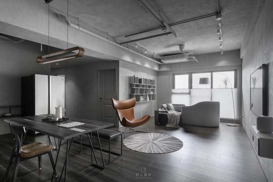 這張照片是一間現代風格的客廳,最顯眼的是中間的棕色皮革沙發,沙發的造型獨特,帶有現代感的設計元素,搭配上簡約的灰白色牆面和地板,營造出沉穩舒適的氛圍。