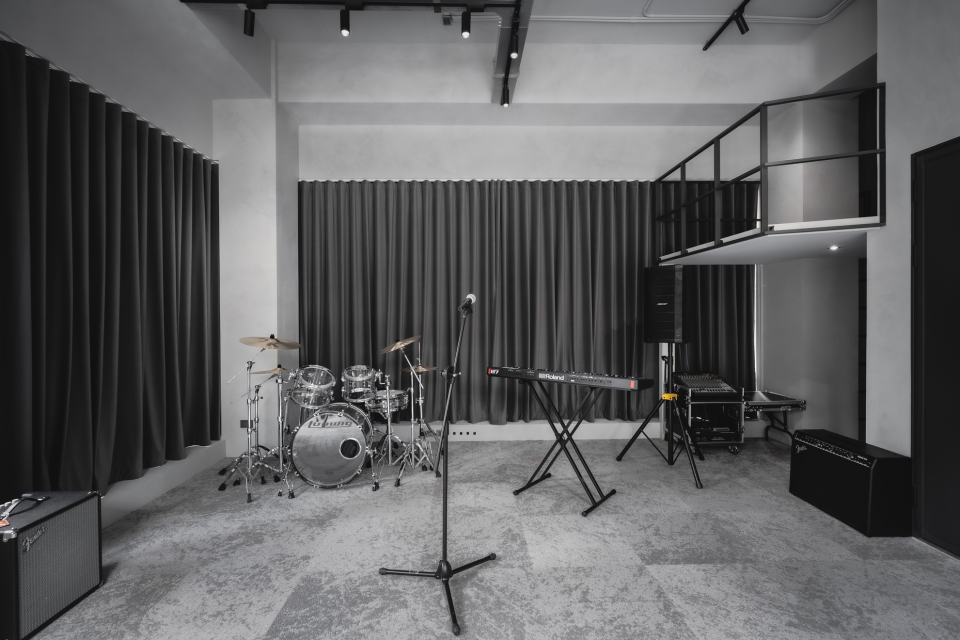 這張「音樂工作室」的照片是,裡面有鼓組、鋼琴、麥克風架和音響。牆上是黑色的窗簾,房間的顏色以灰色和黑色為主,房間的設計很簡單,很適合音樂創作。