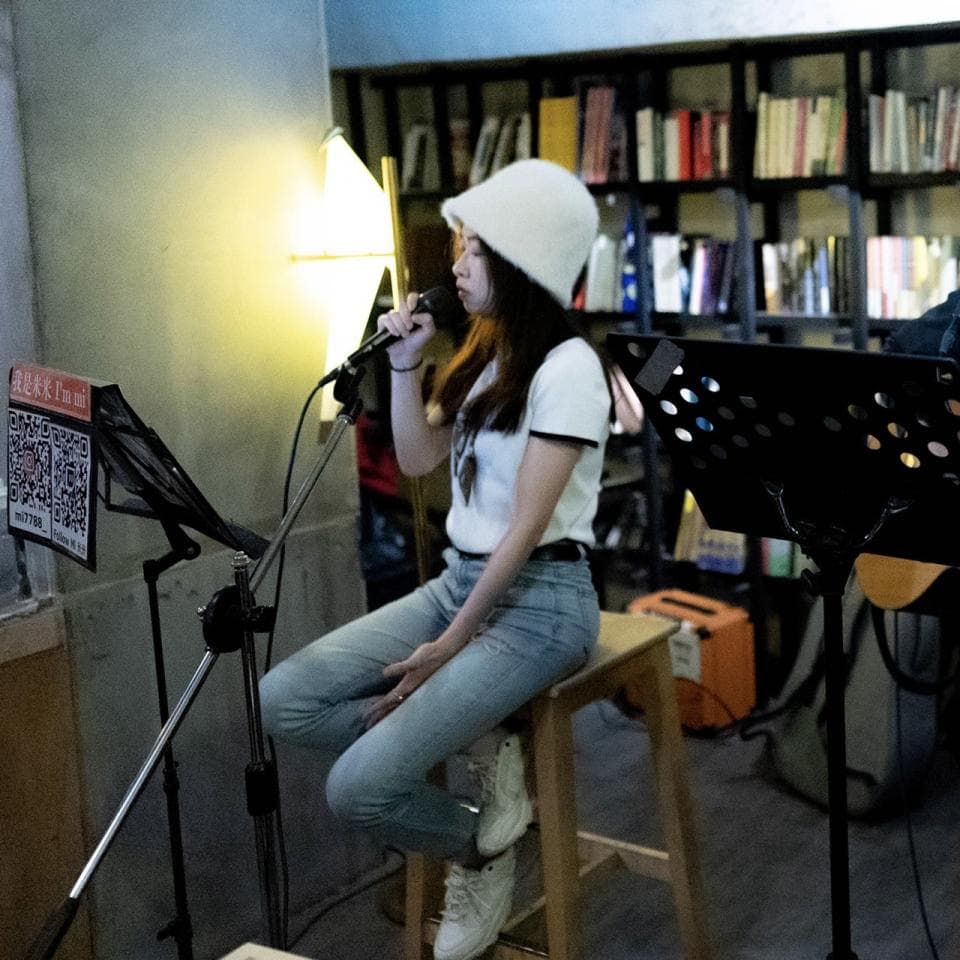 這張照片是一個年輕女孩在唱歌,她戴著白色帽子,穿著白色T恤和牛仔褲,正拿著麥克風唱歌。