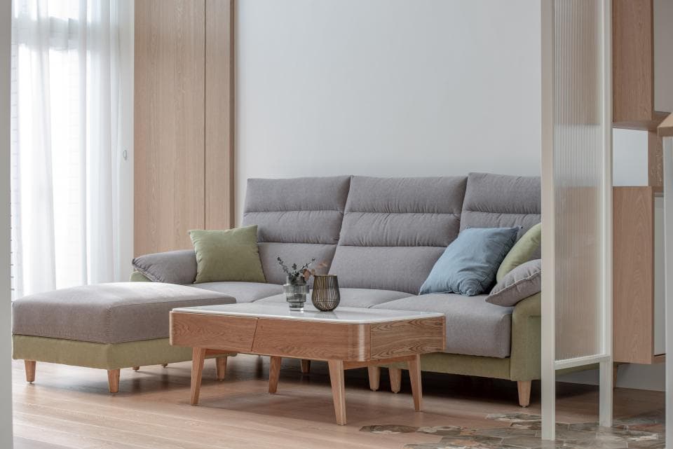 這張照片是一個現代化的客廳,最重要的部分是灰色的沙發和木製的茶几。沙發上有綠色和藍色的抱枕,茶几上有花瓶和綠植,營造出舒適而優雅的氛圍。