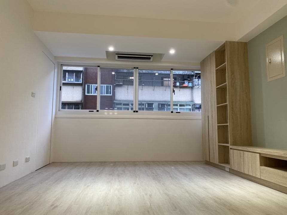 這張照片是一間簡約的房間,最大的特色是房間採光極佳,窗外可以看到一排建築物,陽光灑落在木質地板上,非常溫暖舒適。