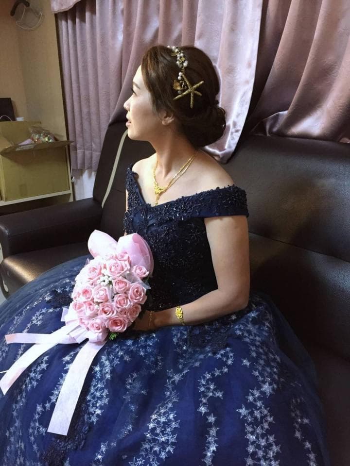 這張「新娘」的照片是一名穿著深藍色婚紗的女性,她手裡拿著一束粉紅色的玫瑰花,頭上戴著一個閃亮的頭飾,看起來非常優雅美麗。