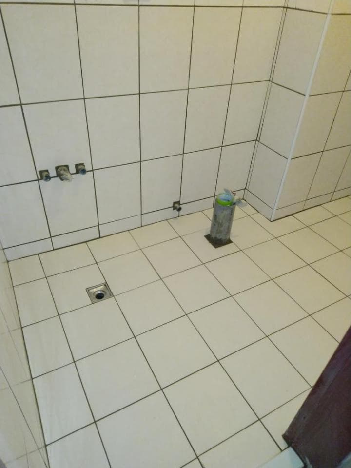 1. 照片顯示一個白色瓷磚浴室,瓷磚地面上有排水口,牆壁上裝有水龍頭,角落放著一個白色塑膠容器