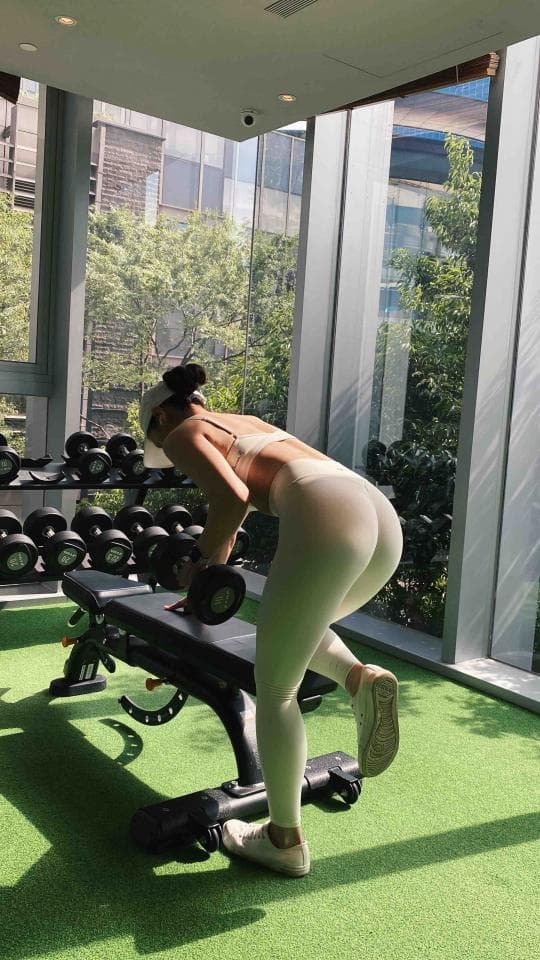 這張照片是一個女孩在健身房舉重。她穿著白色的運動服,正舉起一個啞鈴,專注於鍛鍊。