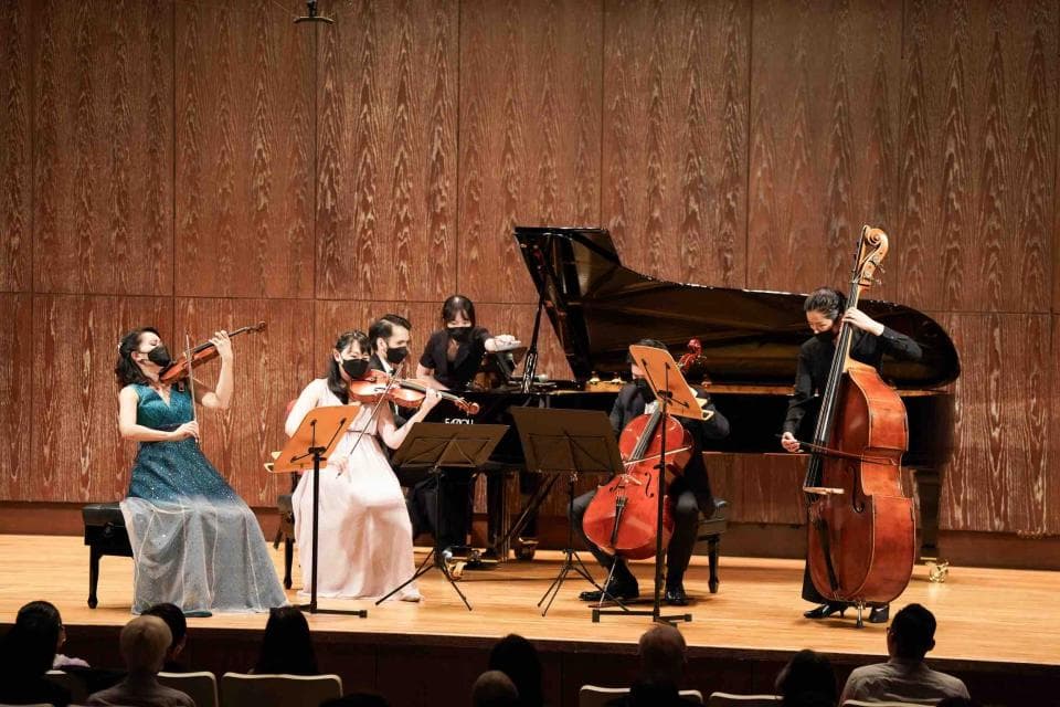 這張「室內弦樂演奏」的照片是一個現場的音樂會,五位音樂家演奏著小提琴、大提琴和低音提琴,背景是一架黑色鋼琴。