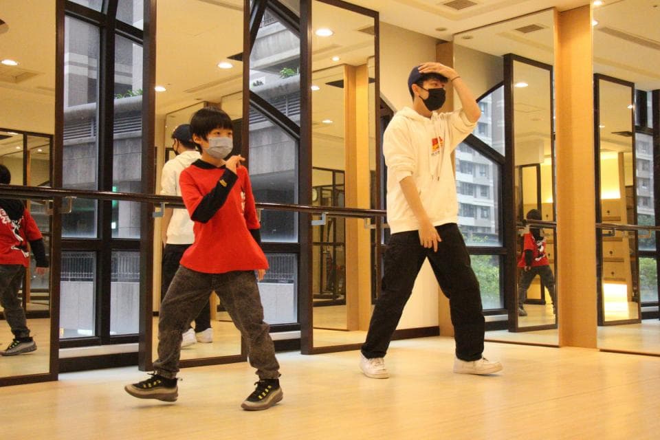 這張「舞蹈教室」的照片是兩個年輕人戴著口罩,在鏡子前面練習跳舞。他們都穿著休閒的衣服,看起來很有活力。