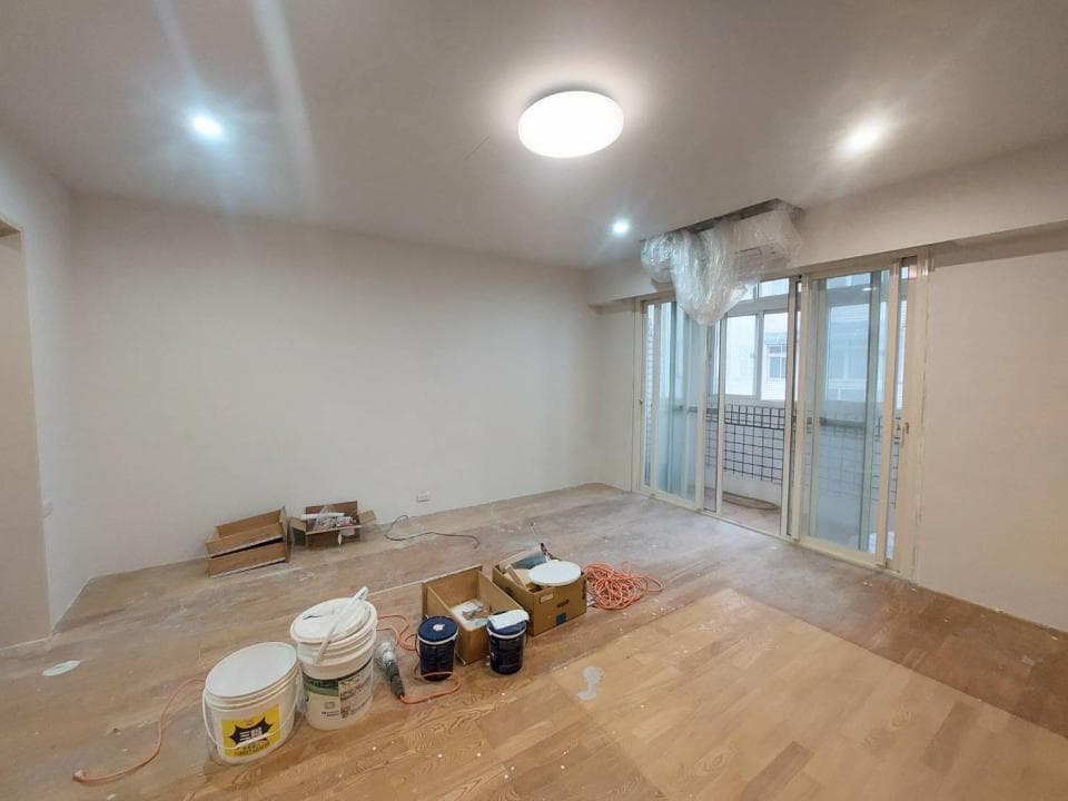 1) 照片顯示一個正在裝修的房子,房間裡有木地板,正在鋪設,地板上有許多裝修用品,像是油漆、工具箱等等,房間內還有窗戶,窗戶外面是陽台