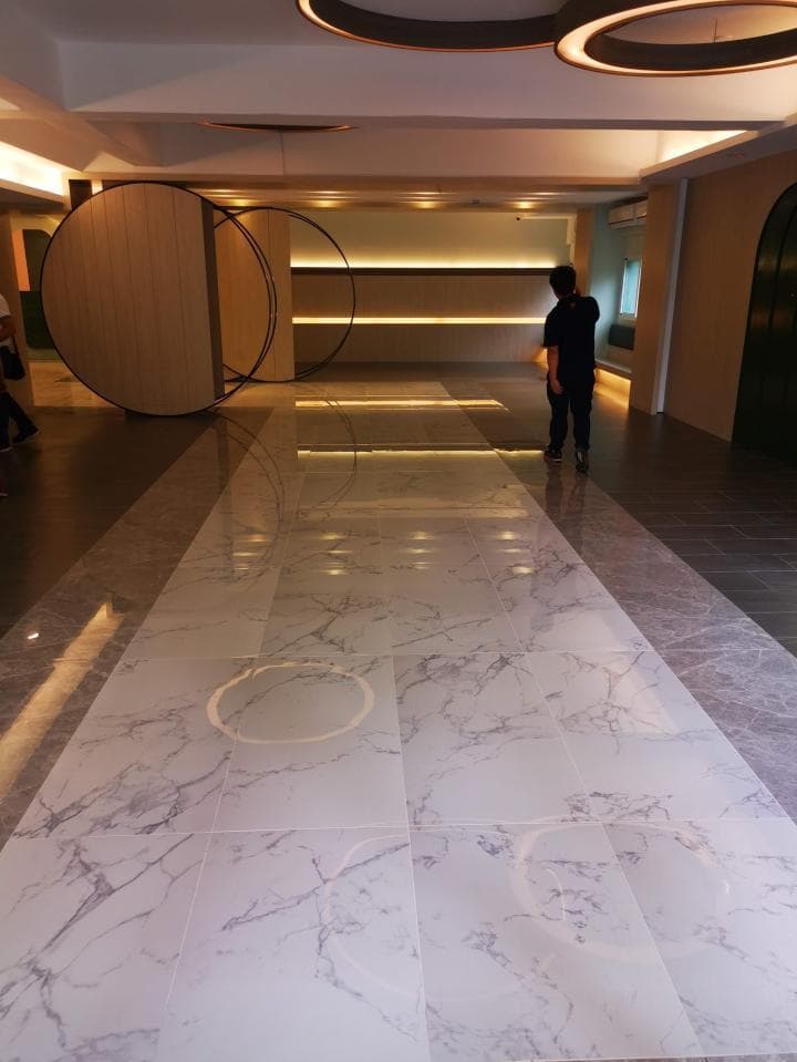 1) 照片展示一個白色大理石地板,地板上有一些灰色紋理,背景是兩側有裝飾品的牆面,以及一個穿著深色衣服的男子站在地板上