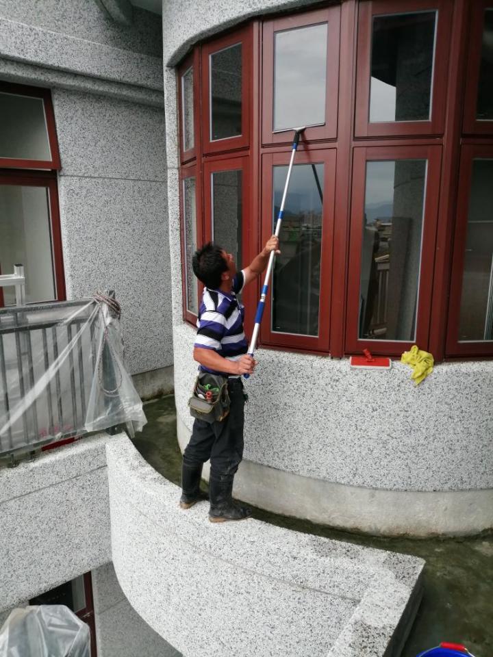 1) 照片顯示一名男子正在擦拭建築物窗戶,使用一根伸縮桿,從側面拍攝