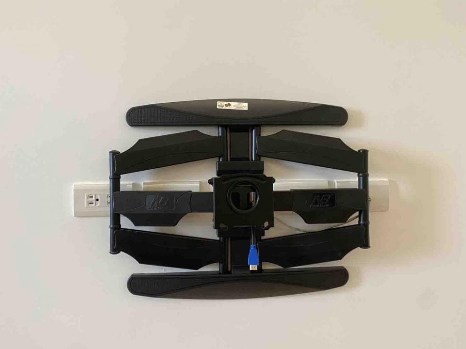 這張照片是牆上安裝的電視支架,由黑色的金屬製成,可以調整電視的角度。支架有四個可調節的關節,可以讓電視旋轉、傾斜和升降。支架上還有一個藍色的插頭,用於連接電源線。