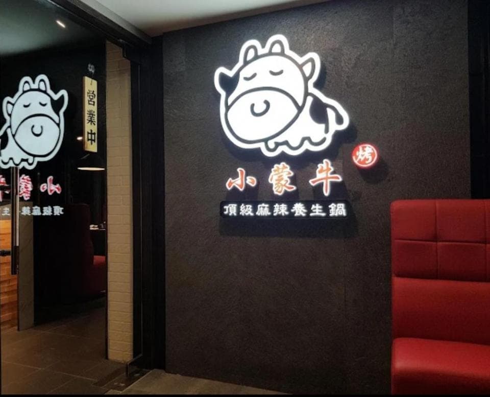 這張「小羔羊」的照片是一家餐廳的招牌,上面有可愛的卡通小牛圖案,還有餐廳的名字和標語。牆壁上還有紅色的座位,看起來很舒適。