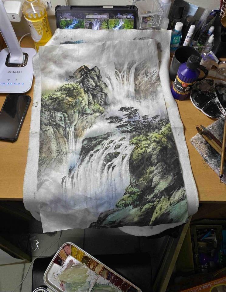 這張照片是一幅中國山水畫,畫中有一座山和一個瀑布,山上有樹木,瀑布從山峰上流下,畫面十分寧靜優美。