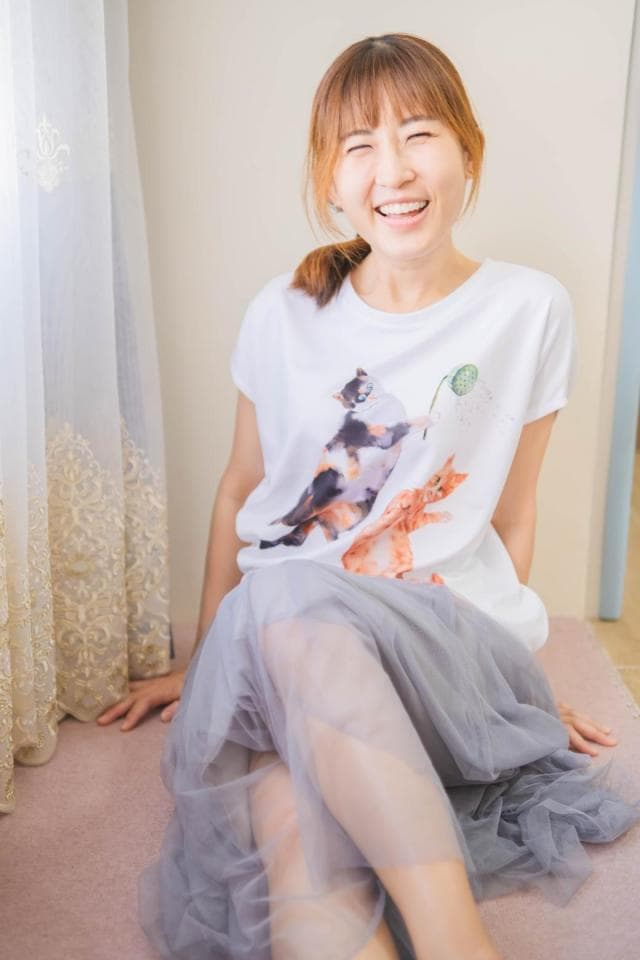 這張「一位年輕女子坐在房間裡,穿著白色印有貓咪圖案的T恤和灰色紗裙,笑容燦爛」的照片是。
